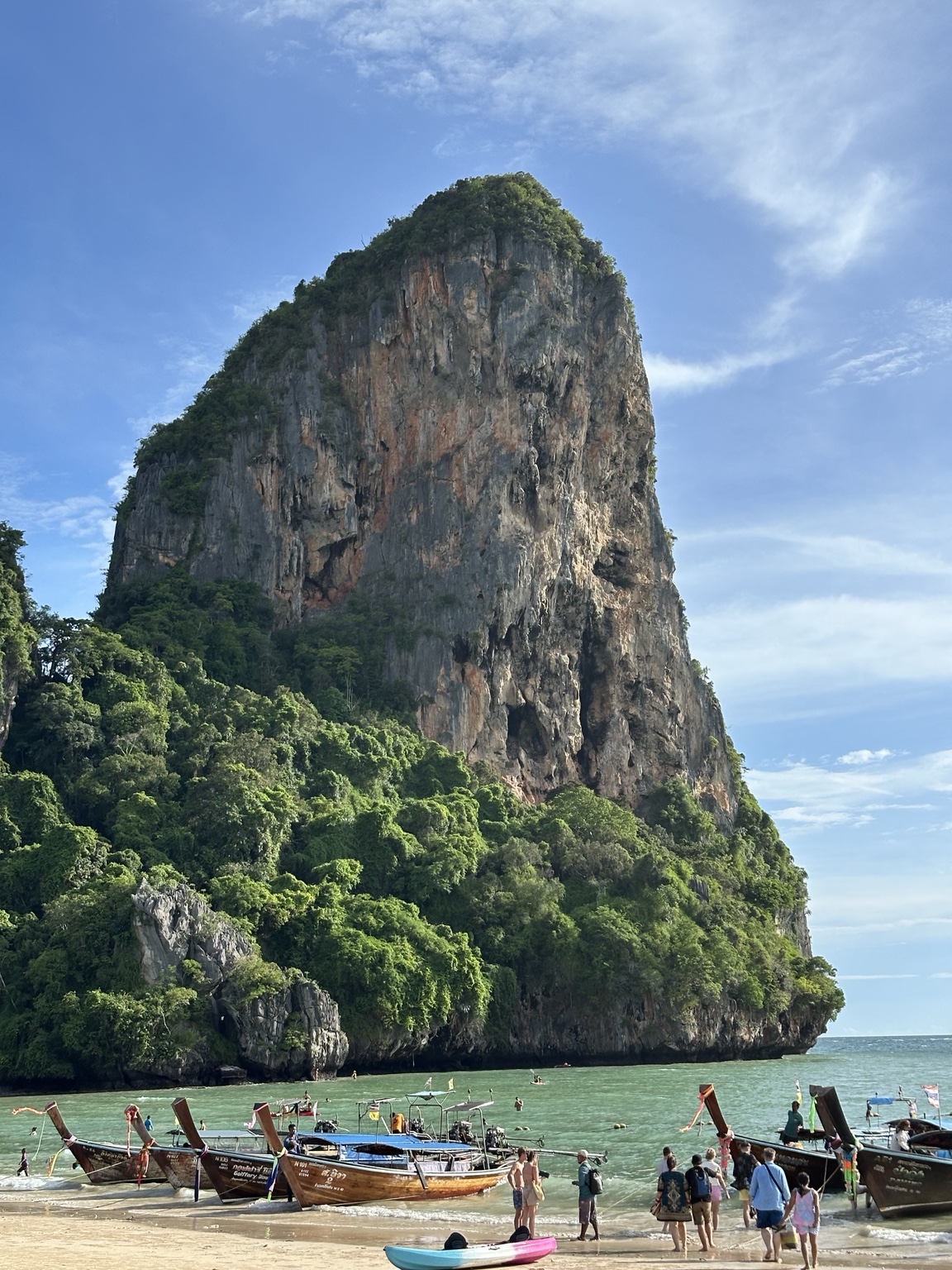 Longtail boats along Railay Beach below a towering limestone cliff